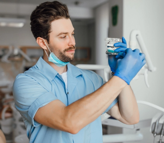 Profesionist dentar de sex masculin purtând mănuși și halat albastru, examinând un model dentar într-o clinică.